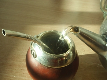 Hot water being added to a traditional yerba mate cup, called a gourd with a metal straw inserted into it. 