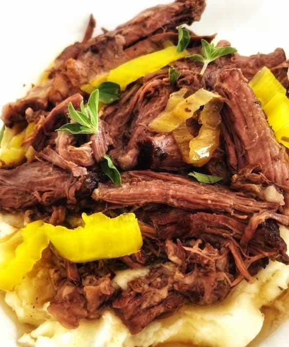 Crockpot Mississippi pot roast with banana peppers served over potatoes. 