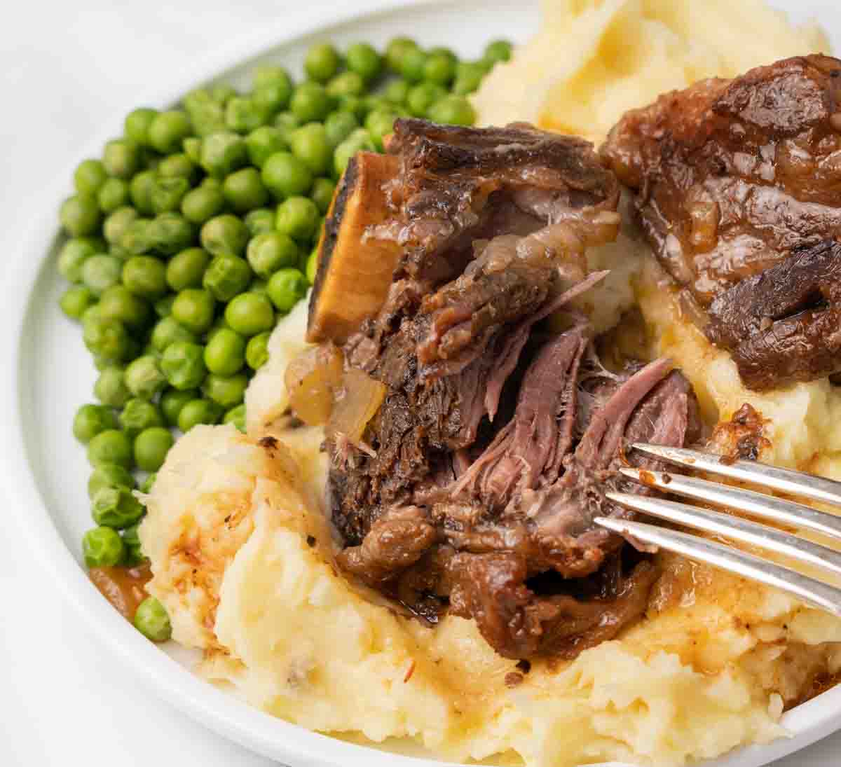 Slow cooker Guiness beef ribs served over mashed potatoes with a side of green peas. 