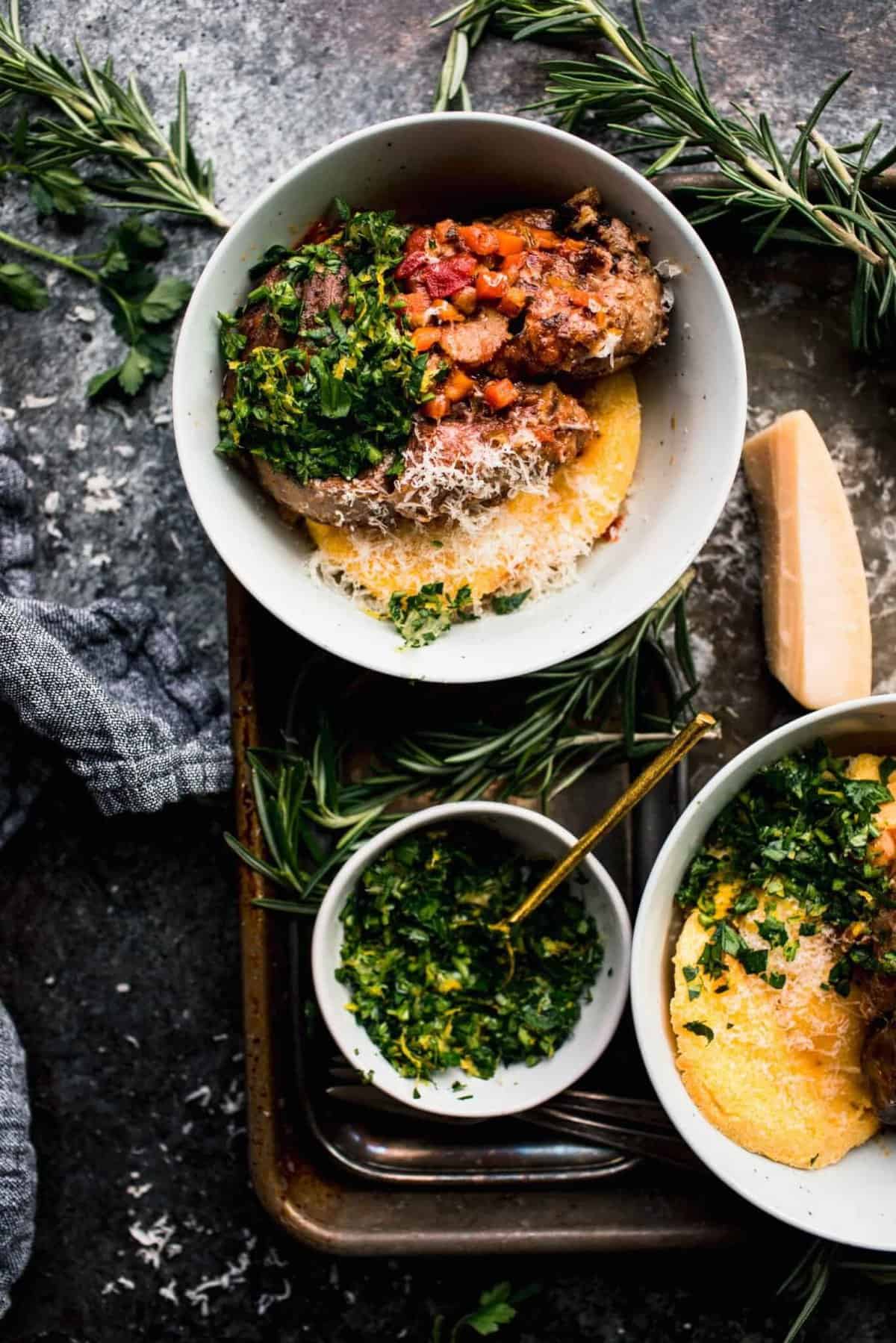 Slow cooker osso buco in a bowl with a sid of greens and polenta. 