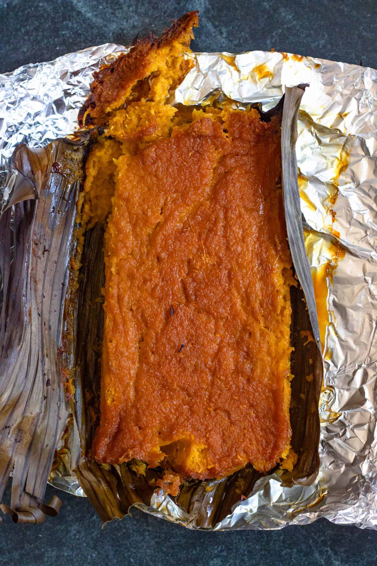 Just baked buatoro in a loaf pan with the banana leaf pulled away to show the dense cake. This dessert comes from Kiribati. 