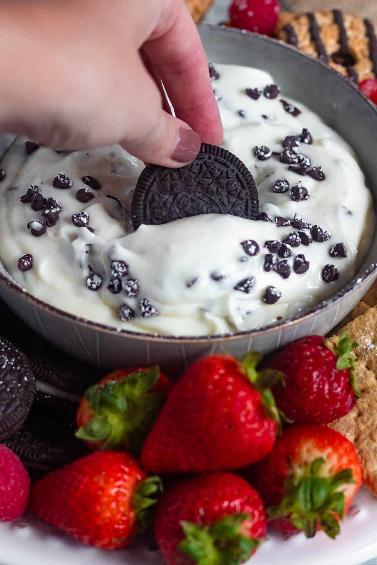 Hand dipping an oreo into a bowl of cannoli dip. 