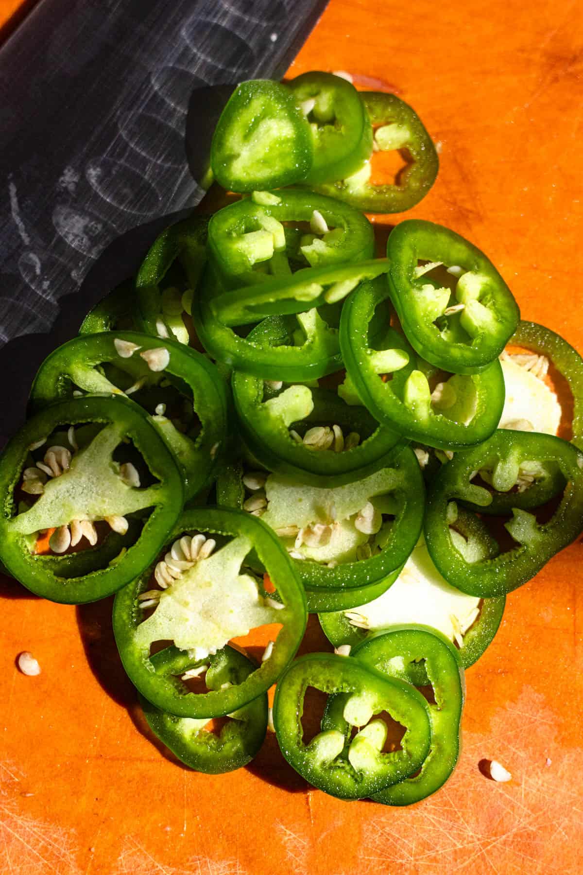 A jalapeno sliced up into round slices on a cutting board next to a chef's knife to add to curtido.