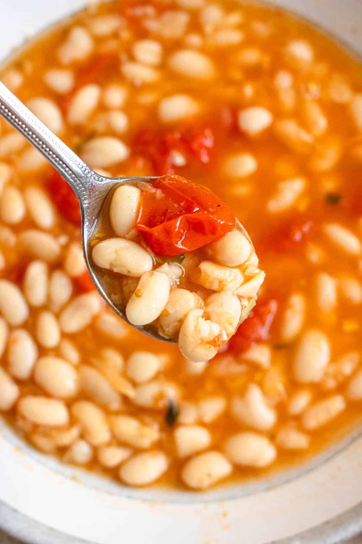 Spoonful of fagioli soup or white bean soup with beans and crushed stewed tomatoes on it. 