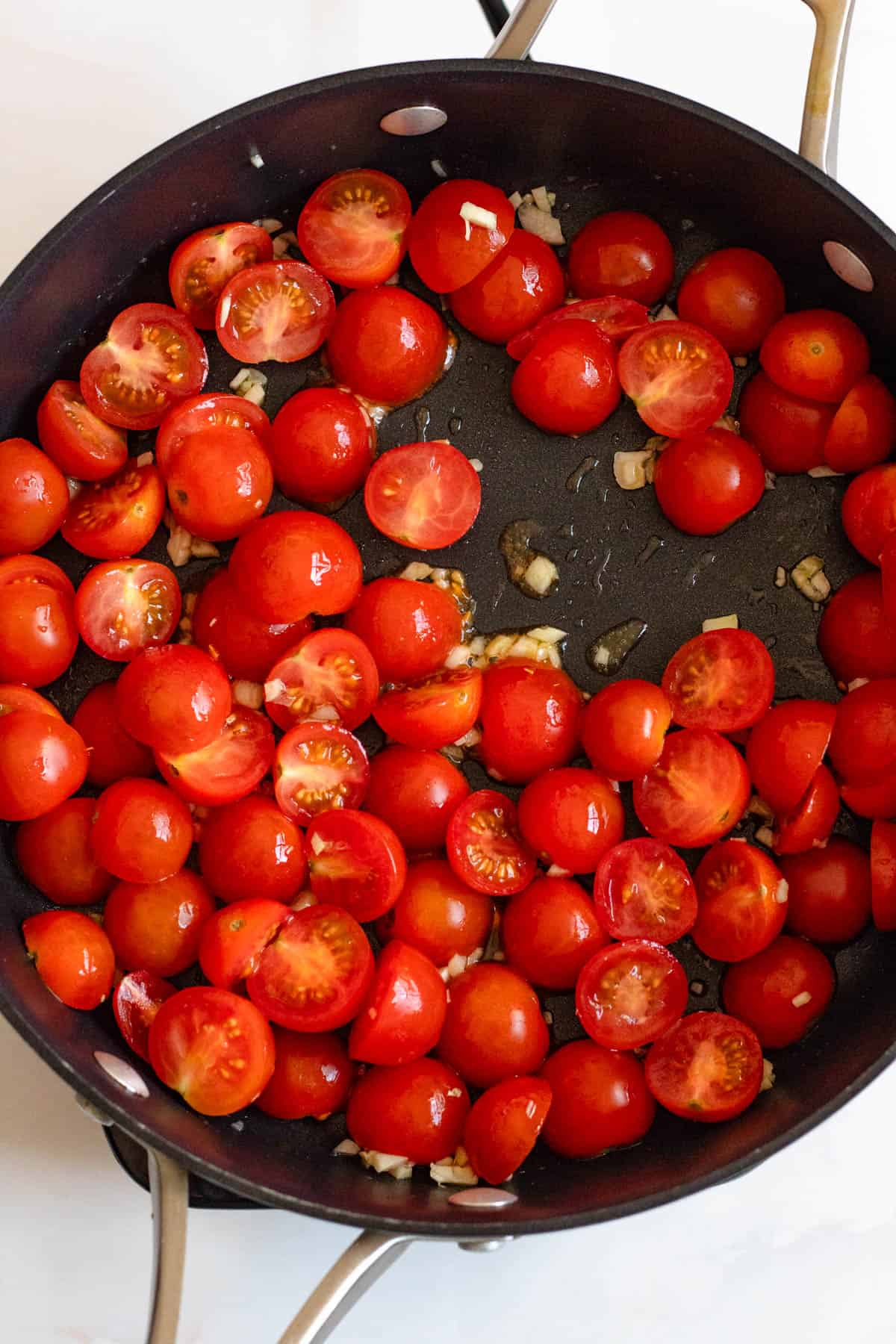 Halved cherry tomatoes added over sauteed garlic in a skillet. 