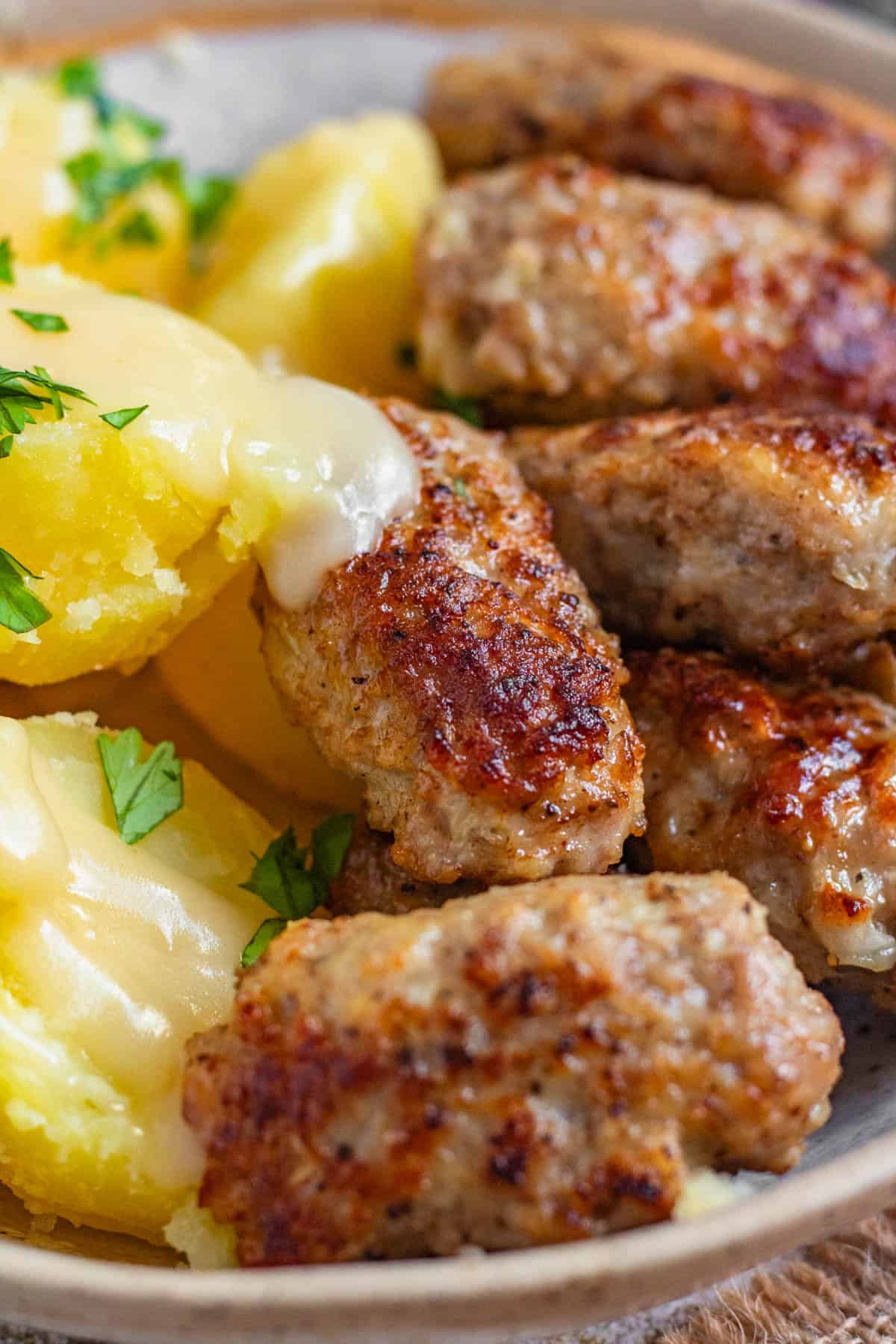 Close up of frikadeller with boiled potatoes and topped with creamy gravy. 