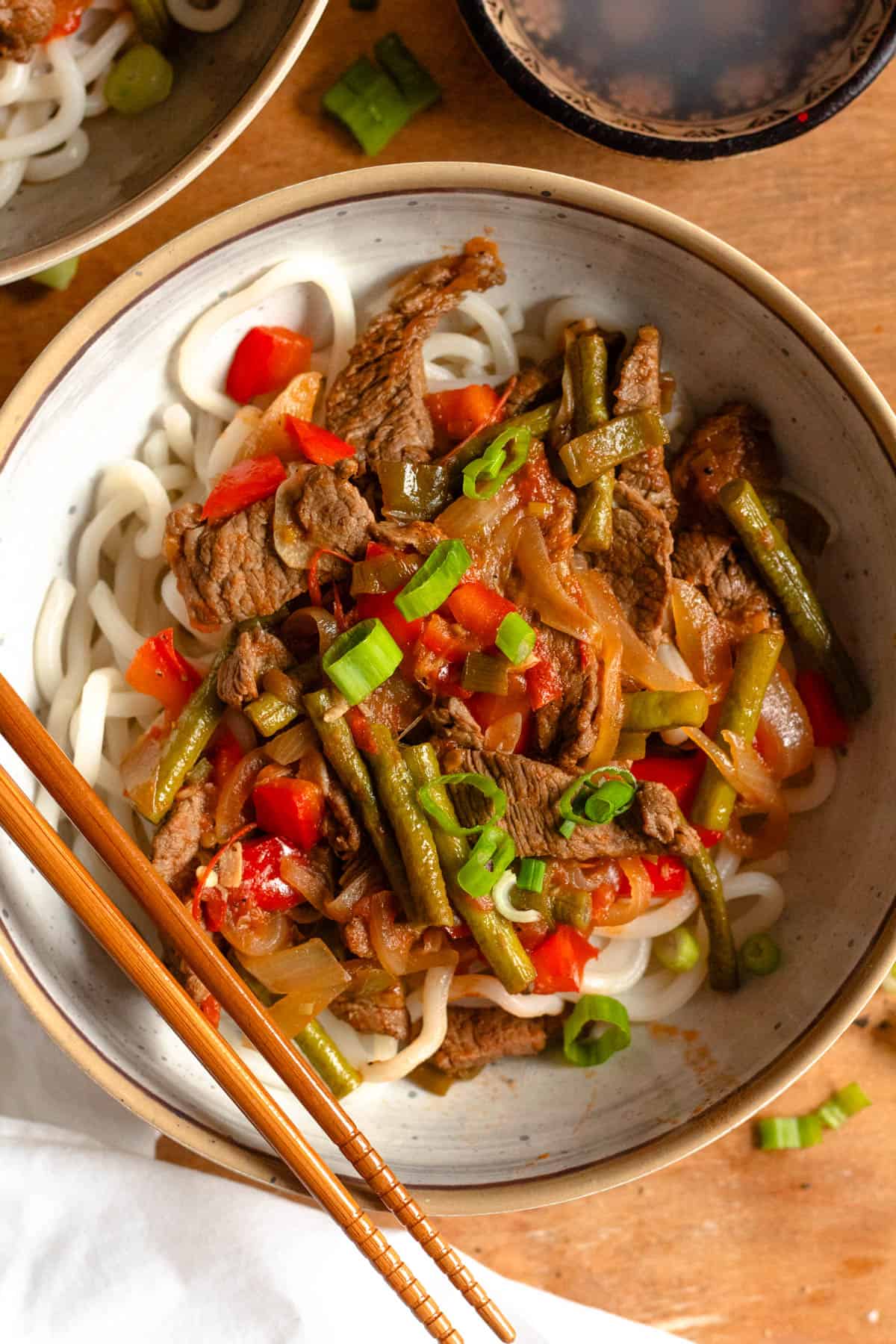 Lagman served over udon noodles and garnished with sliced green onions with chopsticks crossing the bowl. 