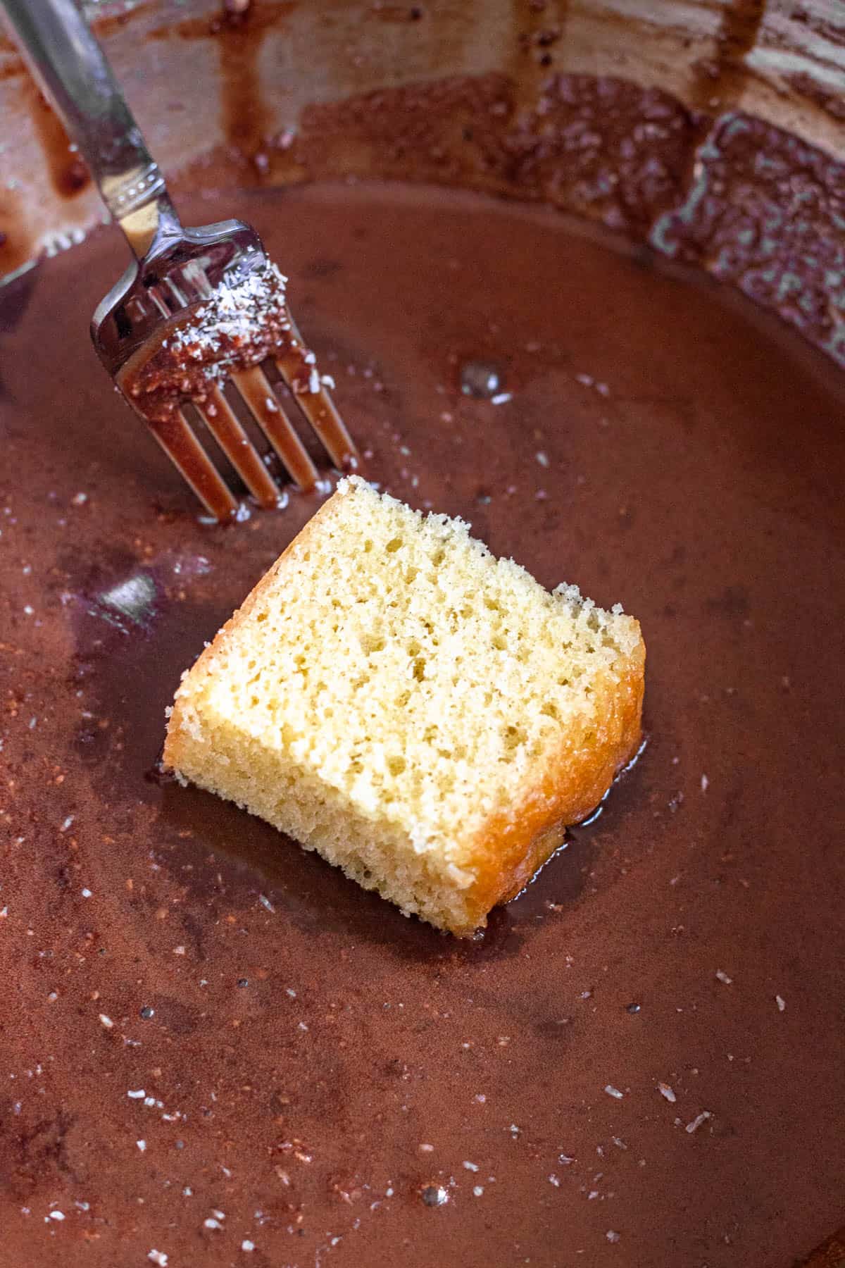 A square piece of cake dipped into a chocolate mixture. 