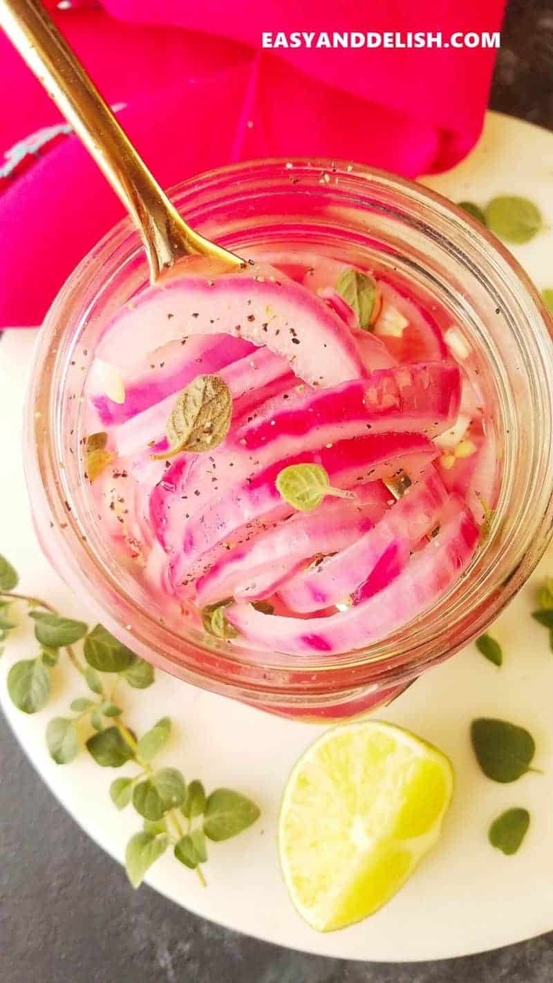 Quick Mexican pickled red onions in a glass jar with a spoon lifting out some to enjoy. 
