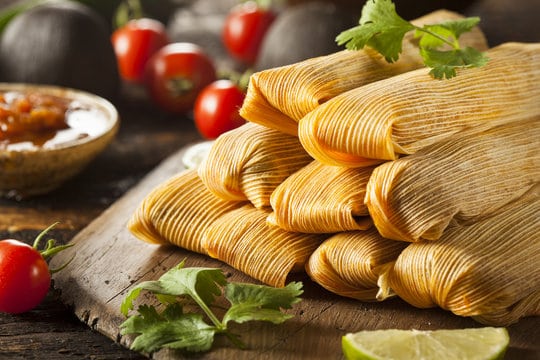 A pile of tamales with cilantro and tomatoes around them. 