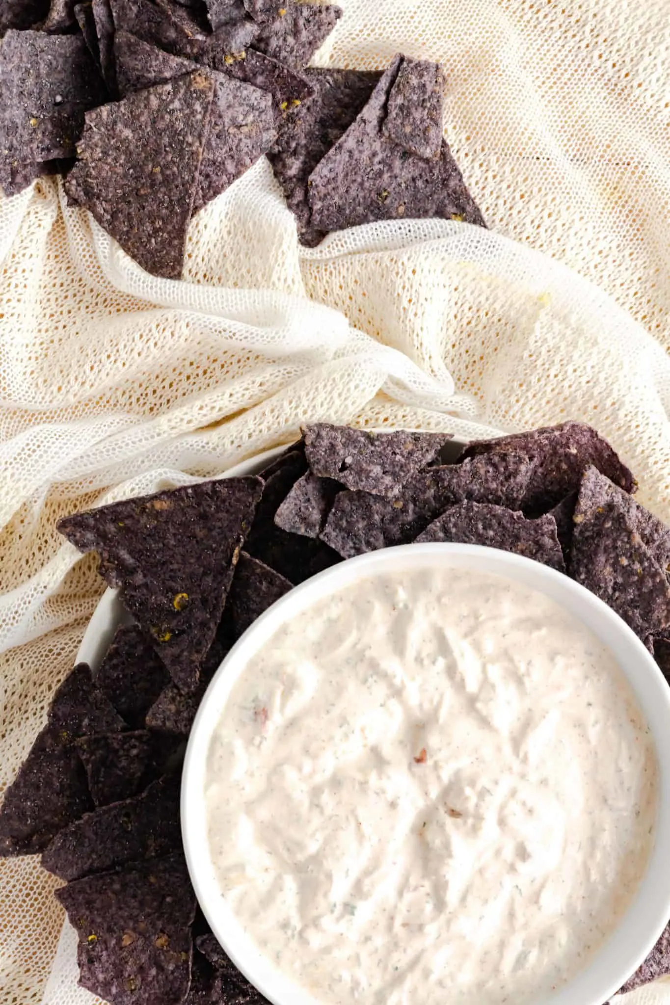 Mexican sour cream dip served in a bowl with blue corn tortilla chips placed around it for dipping. 