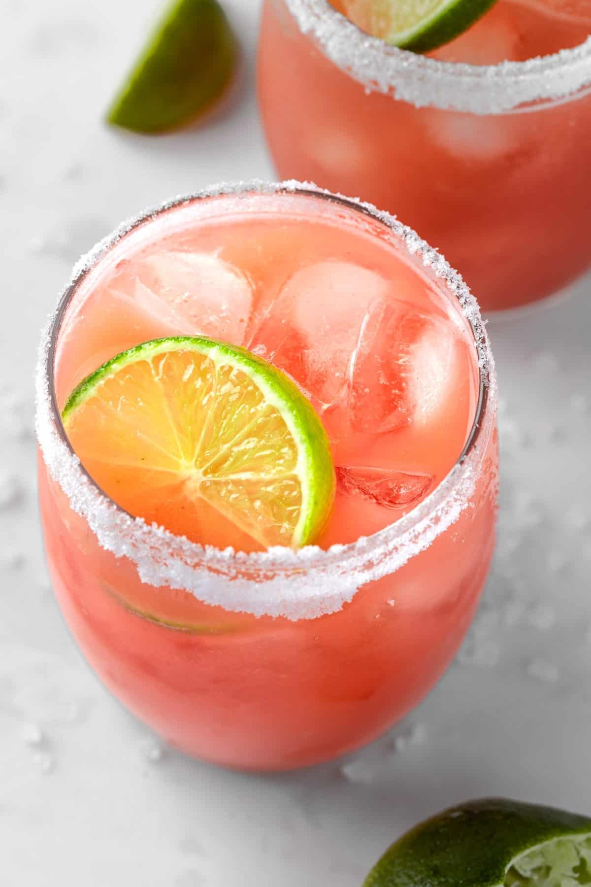 Two glasses of guava margaritas served with a salted rim and a lime wedge. 