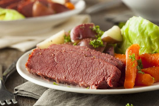 Plate filled with slices of corned beef, cooked carrots and cabbage and red potatoes. 