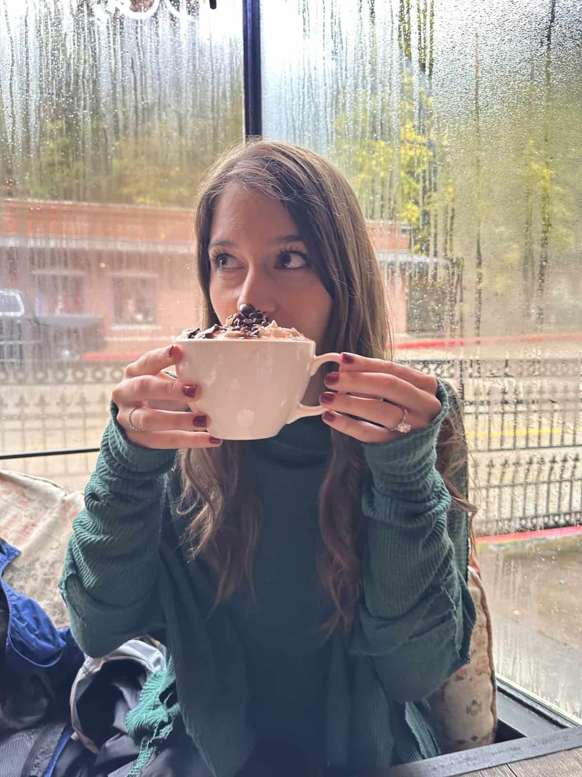a woman drinking a latte in front of a rainy window. 
