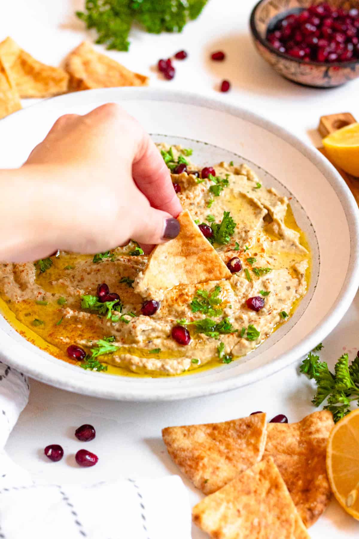 Hand dipping a pita chip in a shallow bowl of baba ganoush.