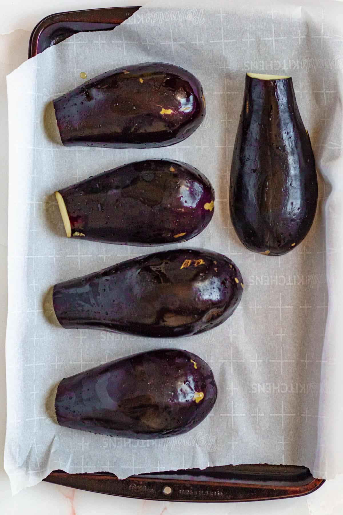 Eggplant resting on parchment paper on a baking sheet.