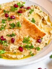 Pomegranate seeds topping baba ganoush with slice of pita bread dipping into it.
