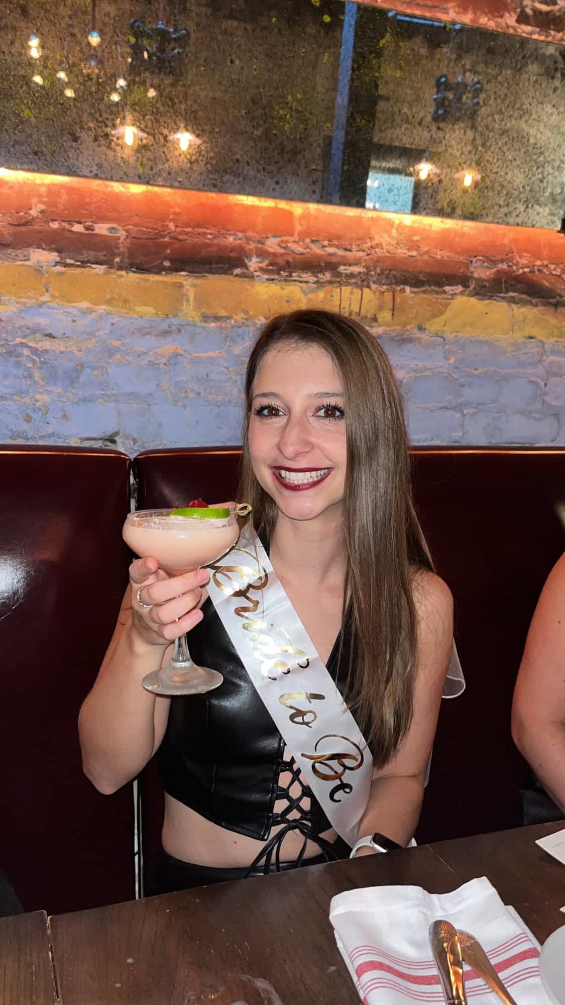 A girl holding a martini glass with a sash on it that says "bride to be". 