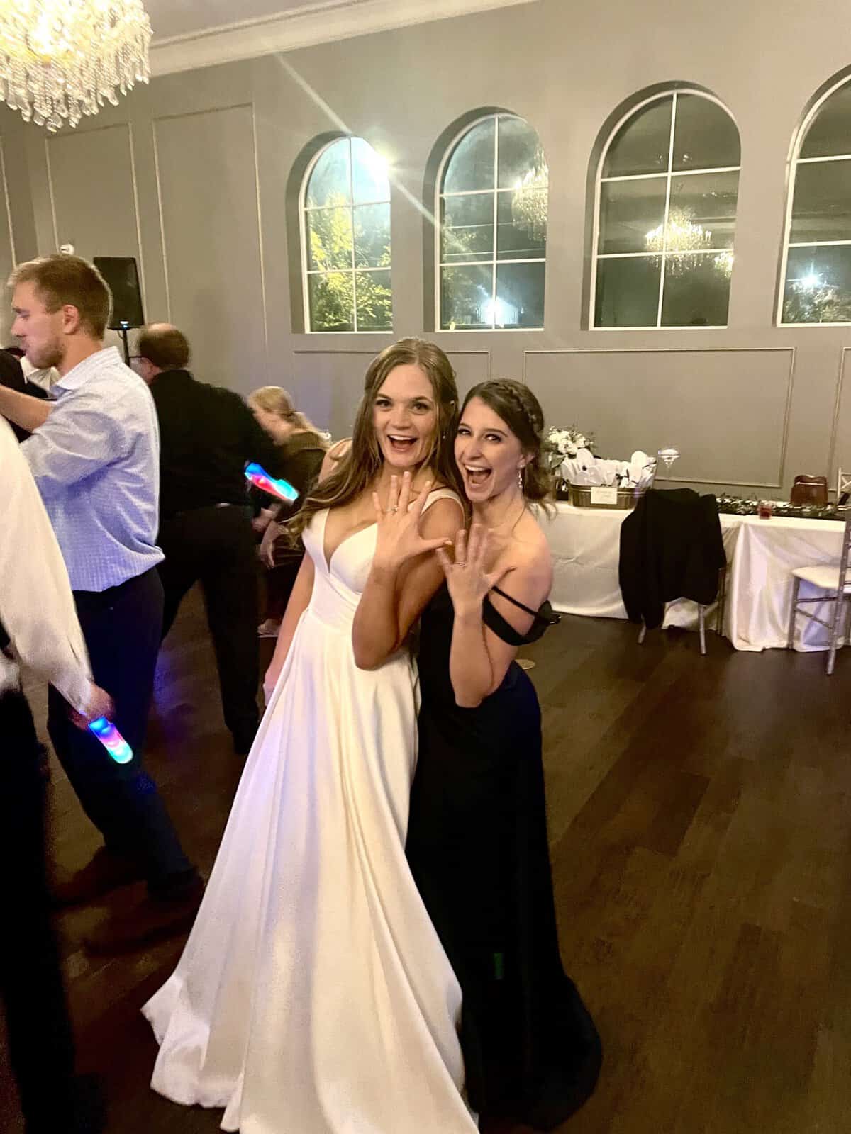 A bride and her bridesmaid showing their ring fingers to the camera.