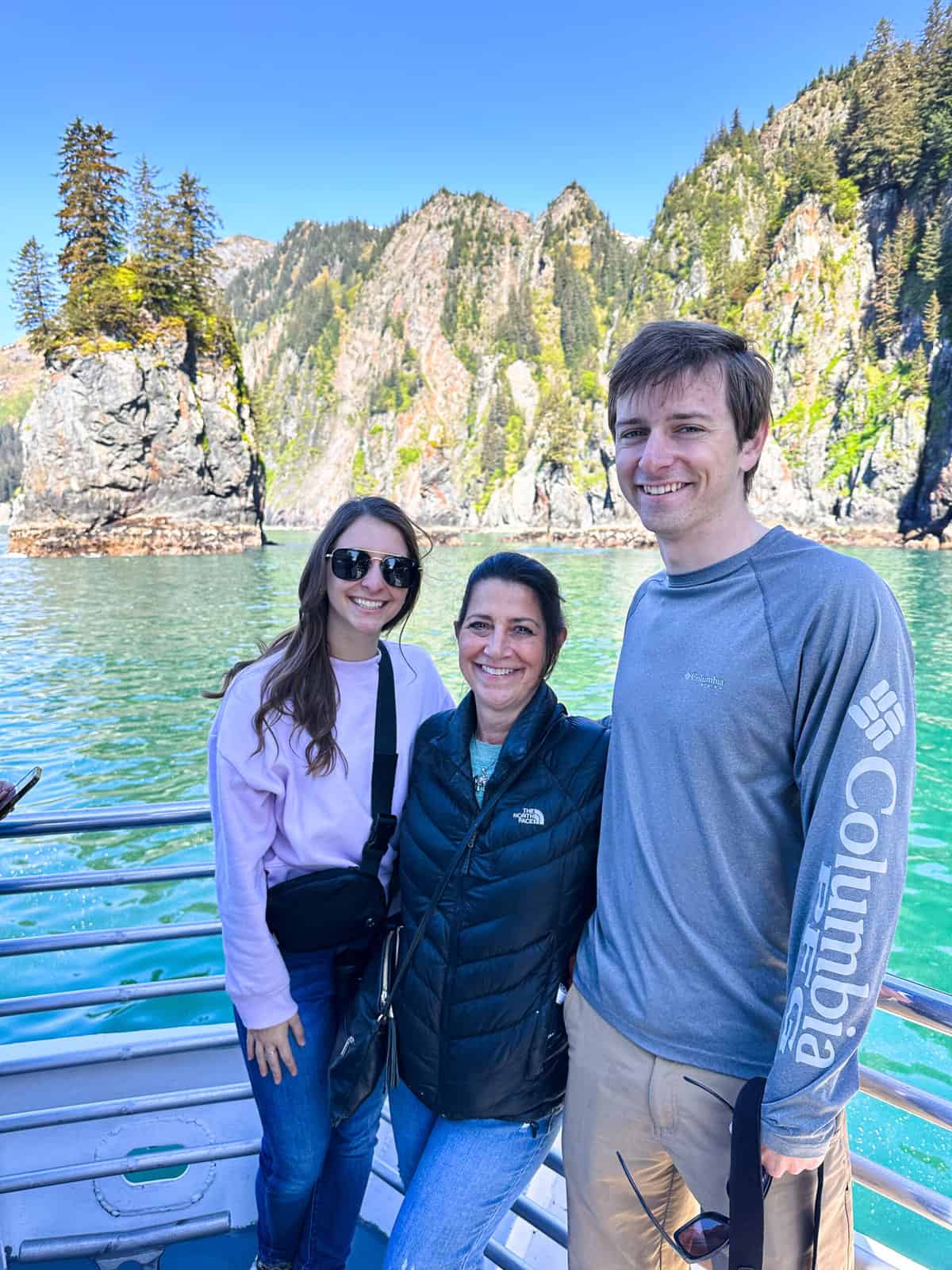 A mom and her two adult children posing in front of Kenai Fjords in Alaska. 