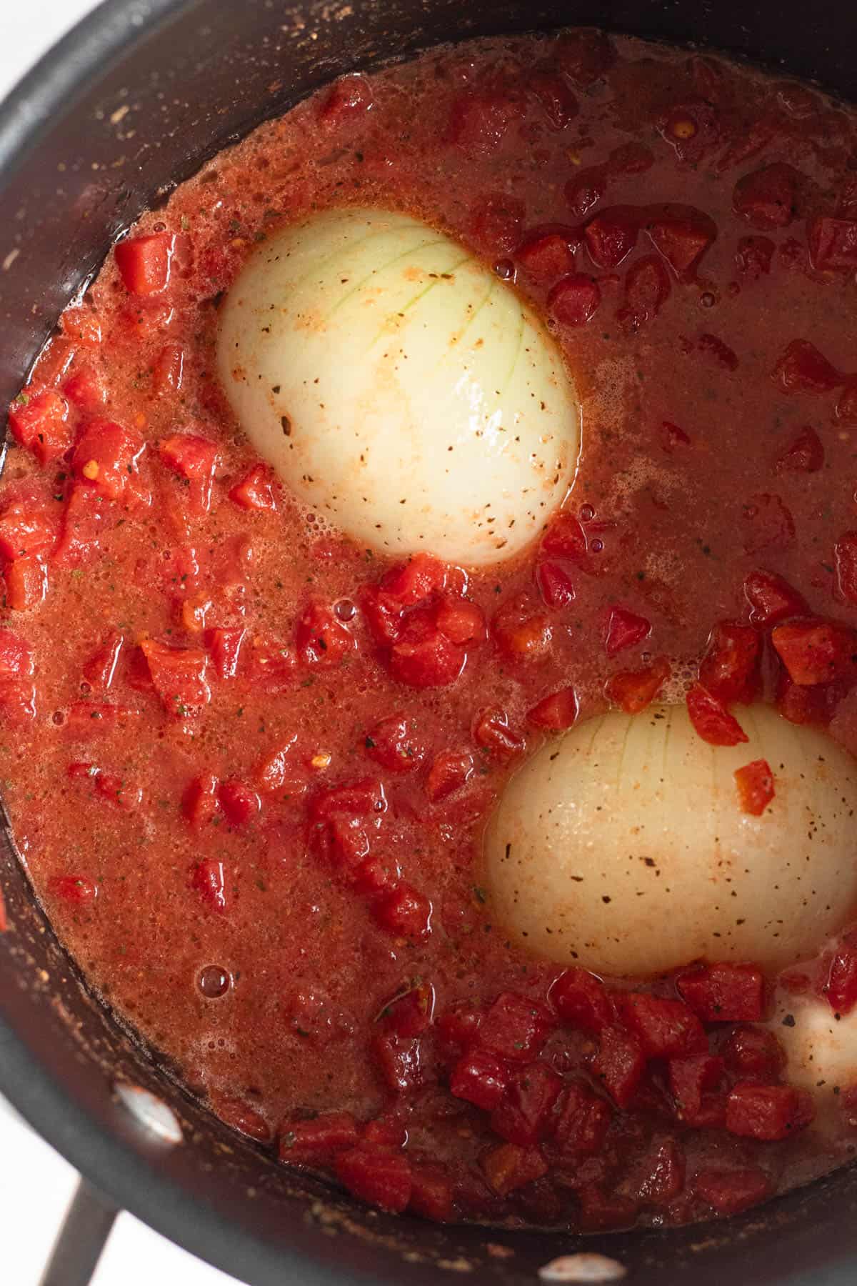 Close up of Marcella Hazan's tomato sauce in a Dutch oven with the halved onions simmering in the sauce. 