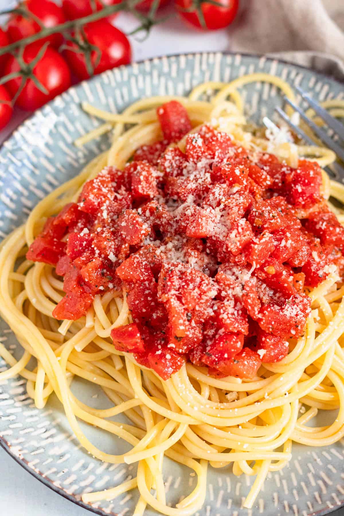 Close up of pasta topped with Marcella Hazan's tomato sauce on a plate with parmesan cheese sprinkled over the top. 