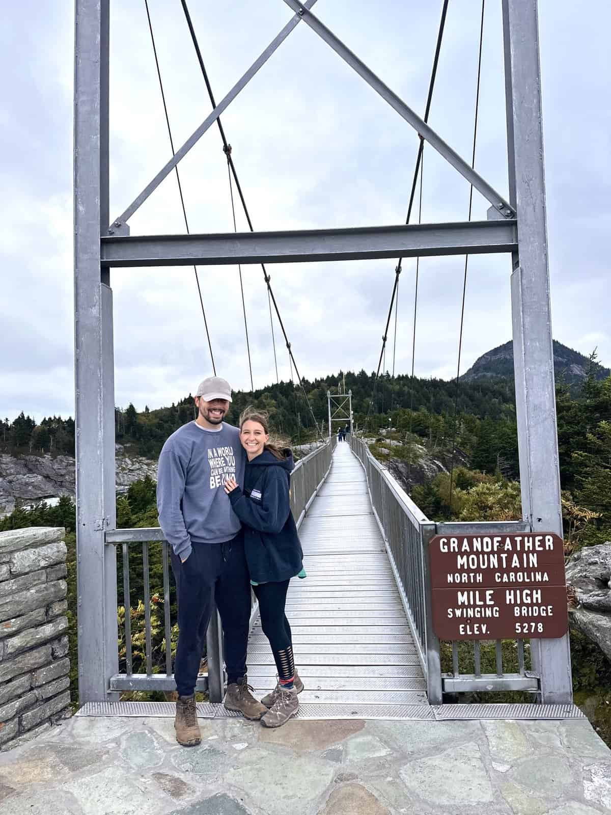 A man and woman posing in front of a metal bridge on a mountain. 