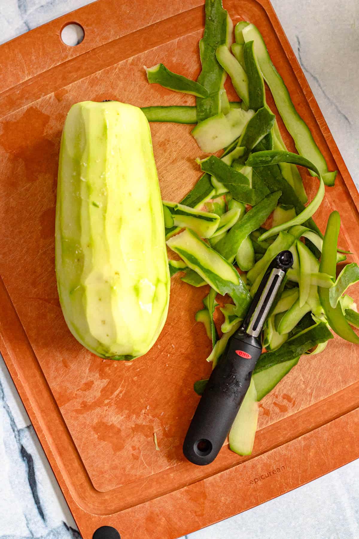 A papaya peeled laying on a cutting board with a vegetable peeler. 