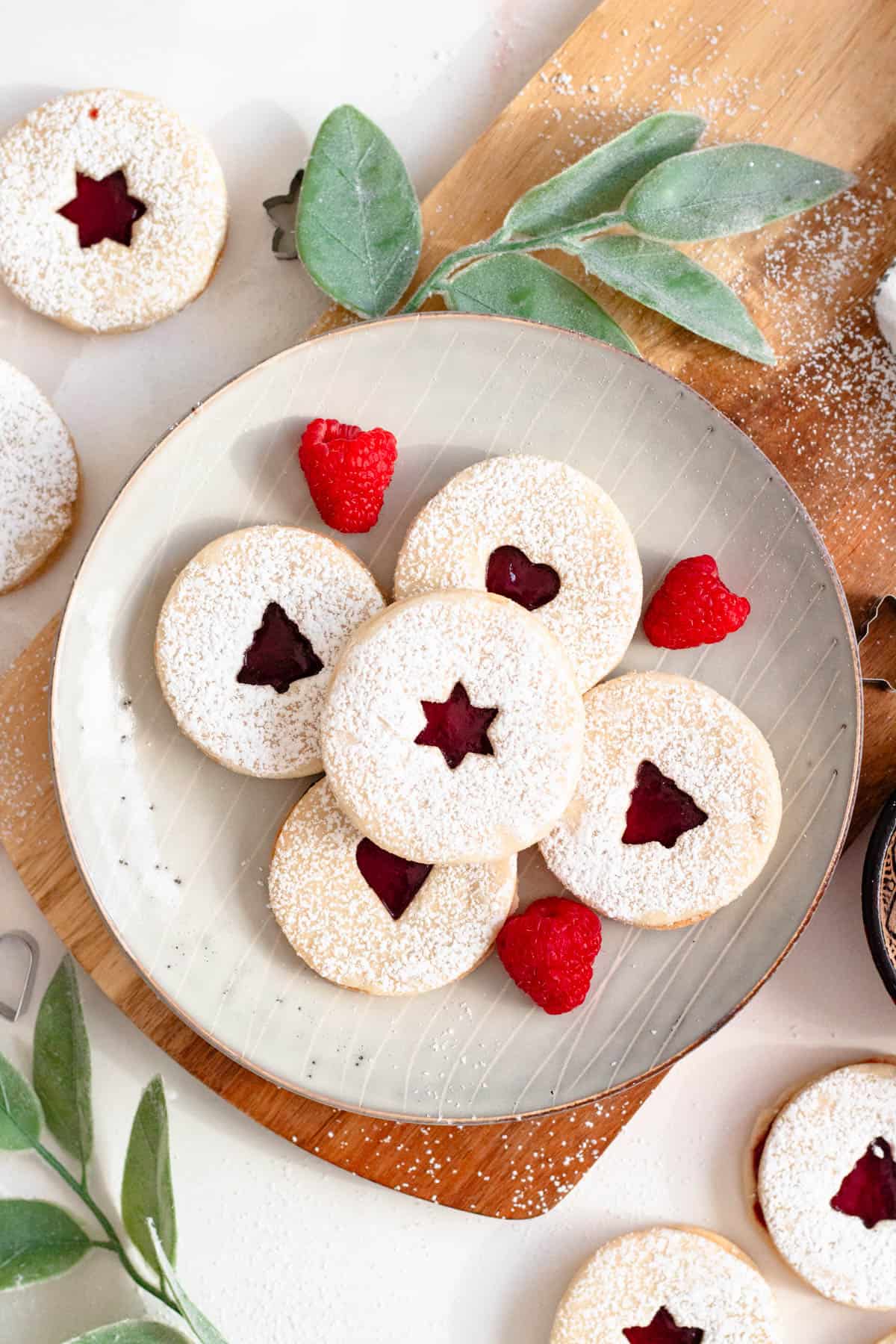 Sable cookies with jam stacked on a plate with fresh raspberries garnished beside them. 