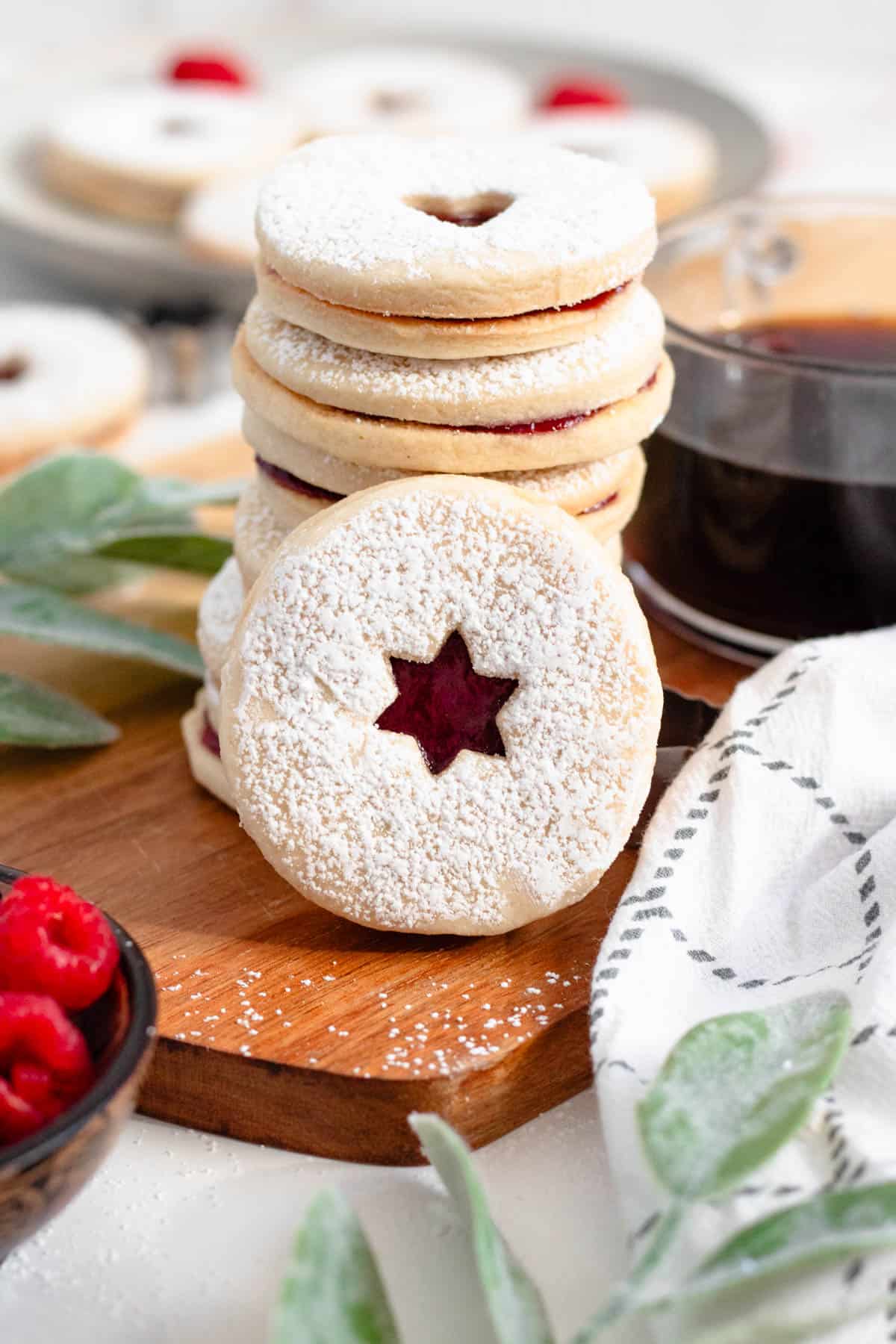 A stack of shortbread cookies with jam and one leaning up against them to show the star cutout and raspberry jam peaking out. 