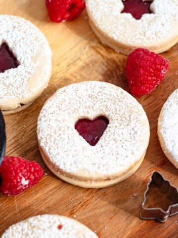 A shortbread cookie, or sable, sitting on a wooden cutting board surrounded by raspberries