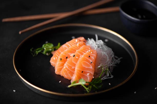 Thin slices of sashimi over cold rice noodles on a plate. 