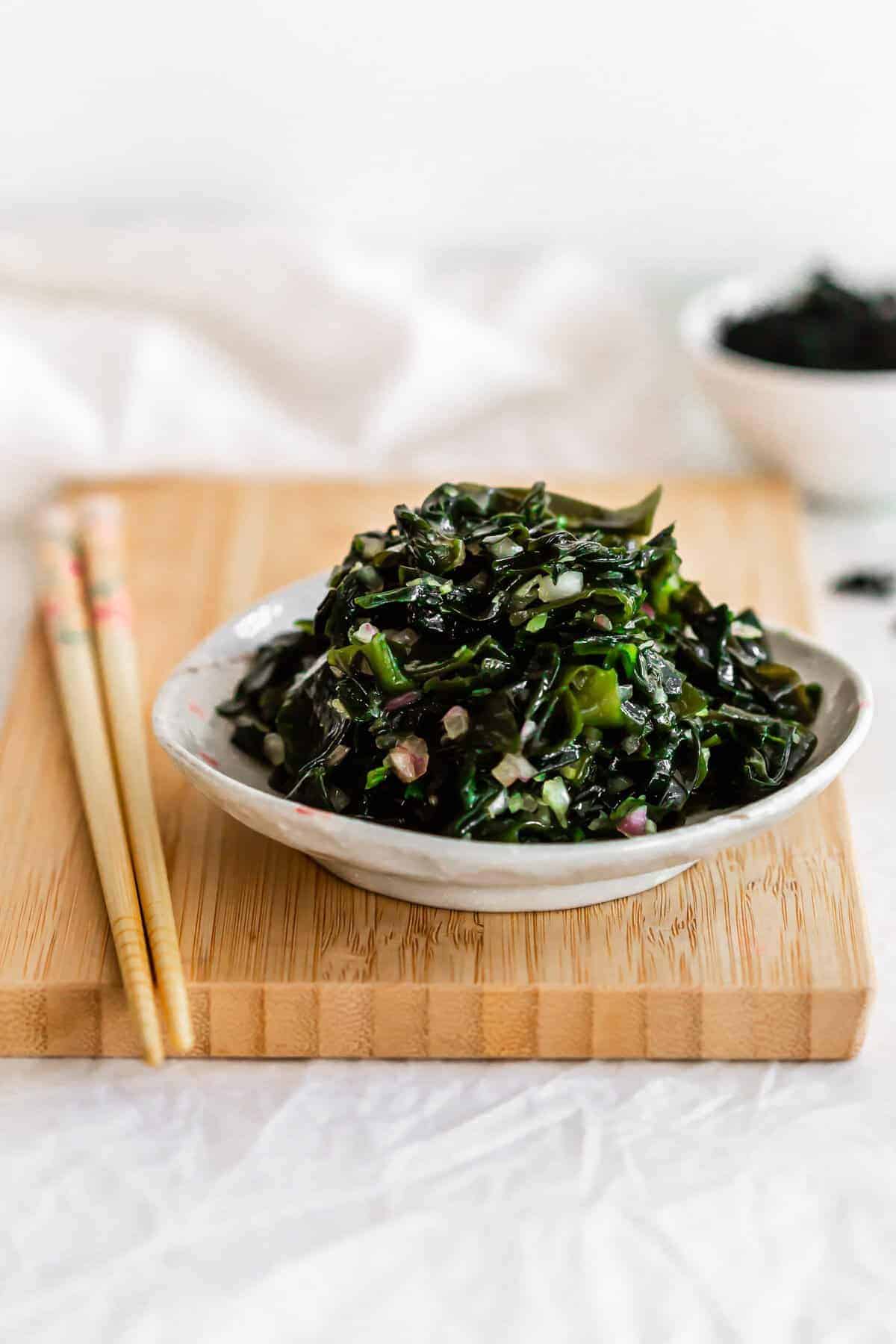 Seaweed salad topping a bowl with chopsticks on the side. 