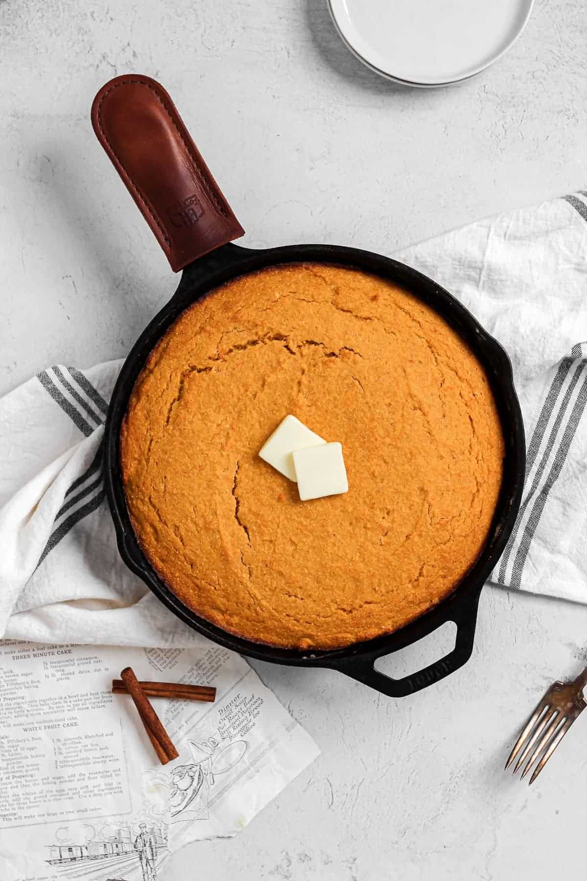 Top view of a skillet of sweet potato cornbread with a couple pats of butter on top. 