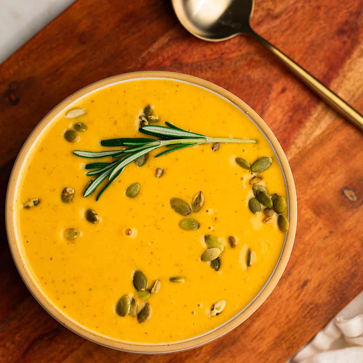 Roasted sweet potato feta soup with rosemary served in a bowl and garnished with fresh rosemary and pumpkin seeds. 