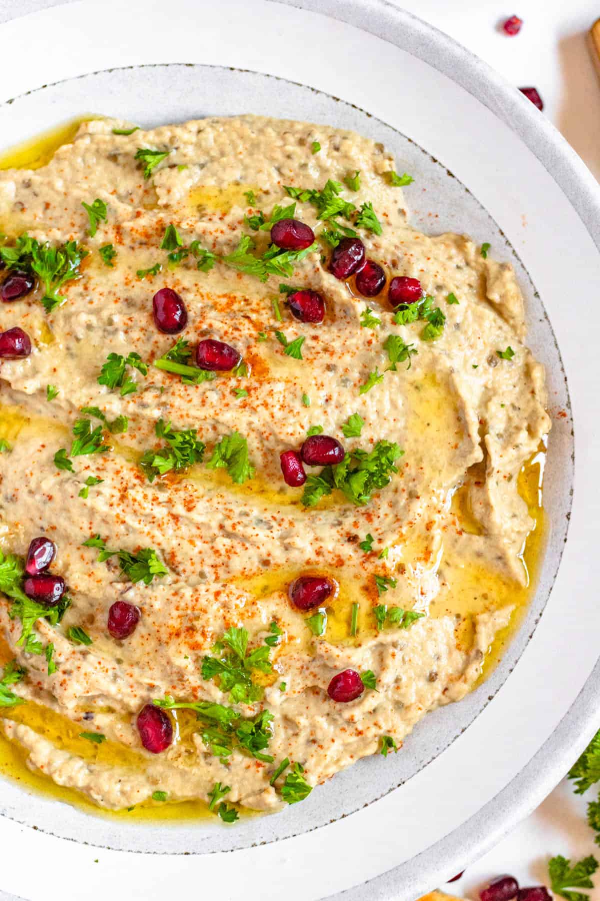 An overhead view of baba ganoush topped with parsley, olive oil, and pomegranate seeds