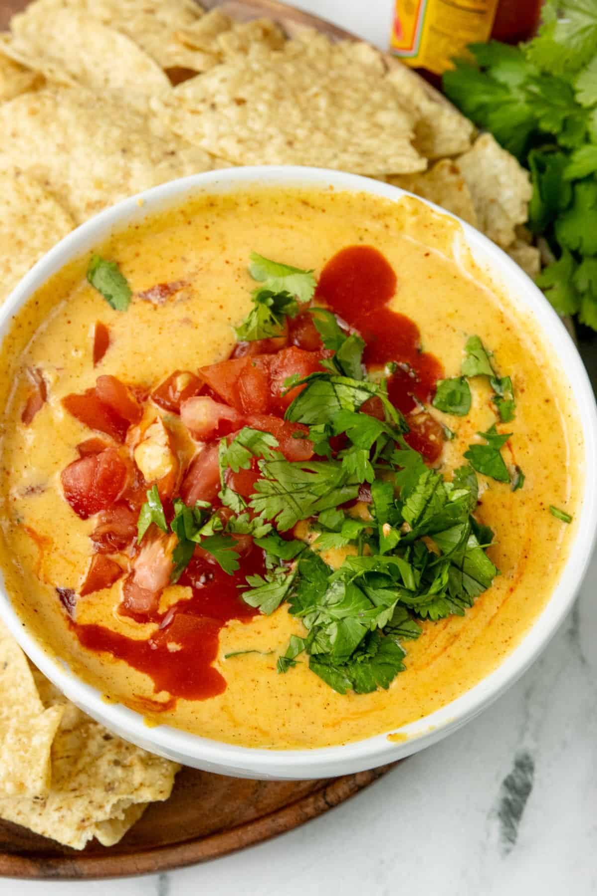 Top view of an easy queso dip served in a bowl and garnished with cilantro and hot sauce with diced fresh tomatoes. 