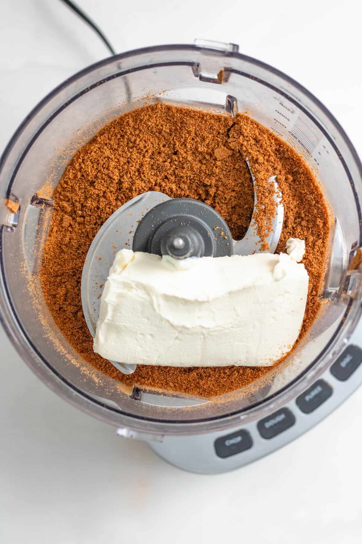 Block of softened cream cheese added to a food processor with crushed gingersnap cookies. 