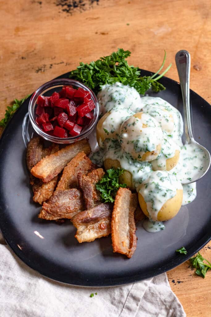 Stegt Flaesk on a plate with pickled beets, parsley sauce, and potatoes.