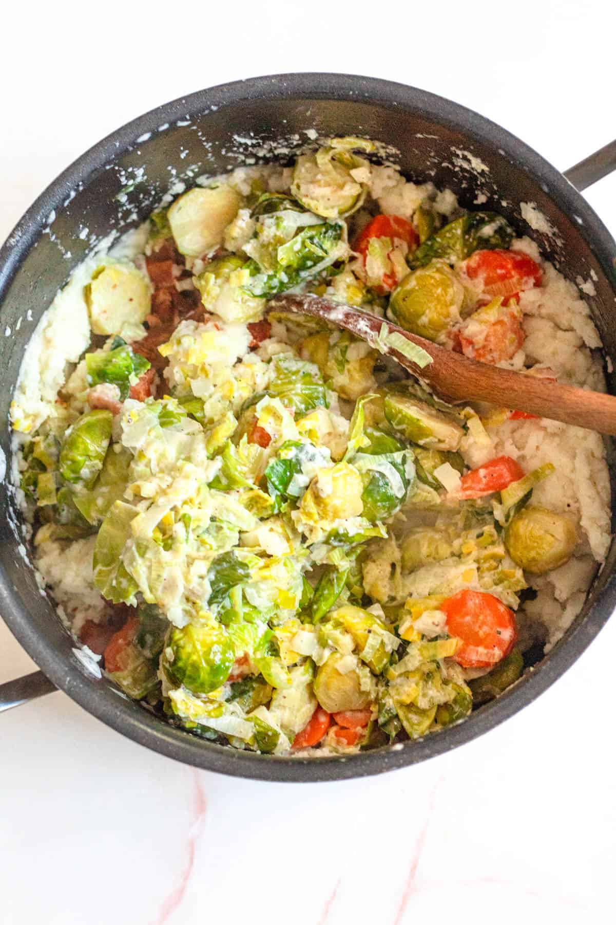 Potatoes and vegetables being mashed together in a pan. 