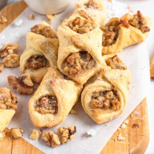 Chopped walnuts laying around a stack of freshly baked walnut cookies that are dusted with powdered sugar, laying on parchment paper.