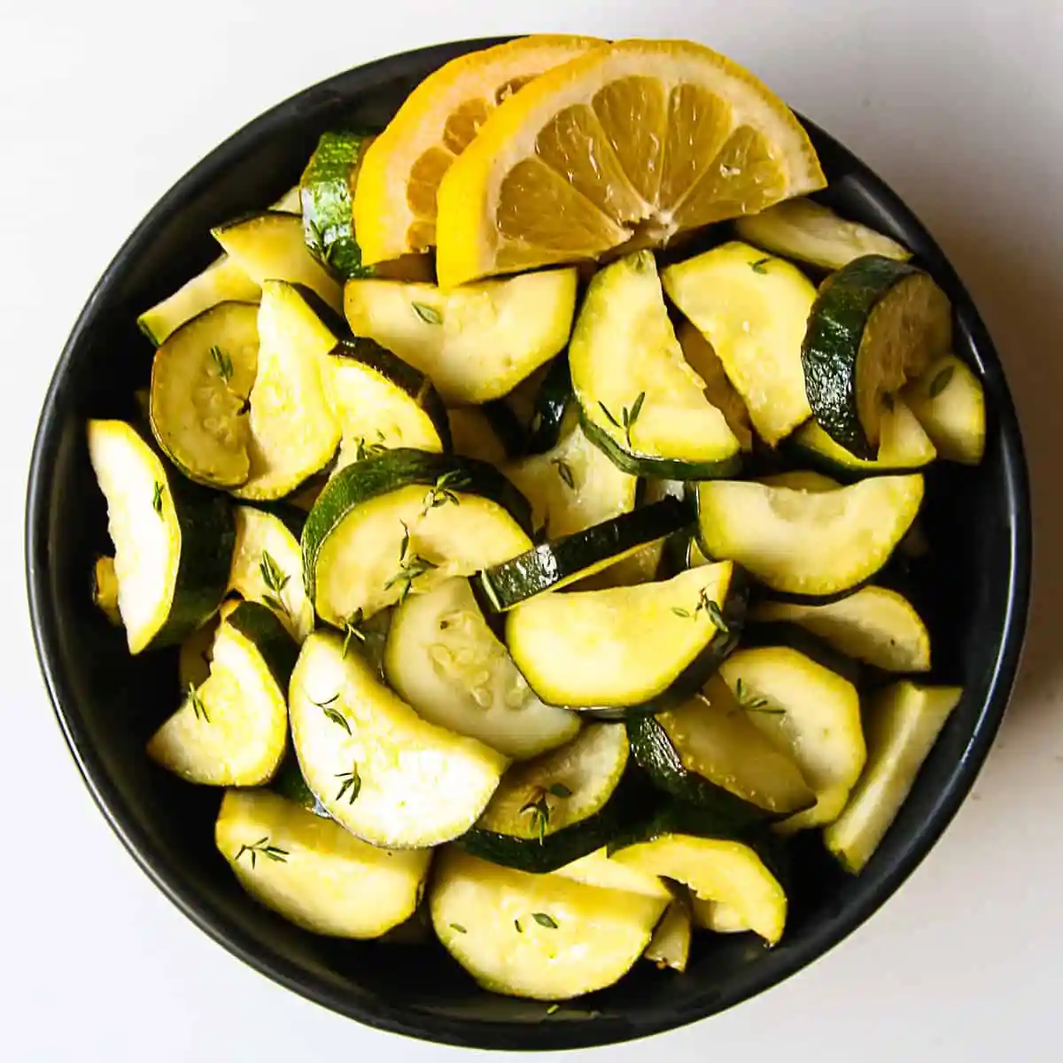 Air fryer zucchini on a plate with lemon wedges garnished on the side. 