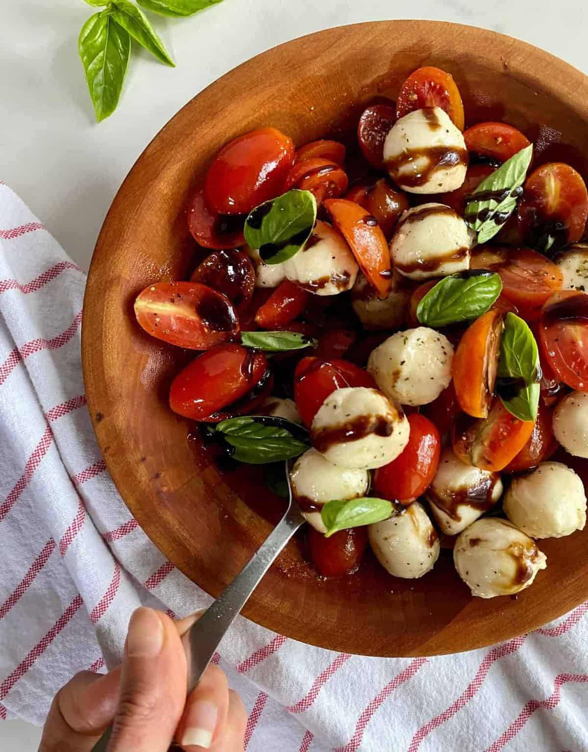 Wooden salad bowl serving bocconcini tomato salad drizzled with balsamic glaze. 