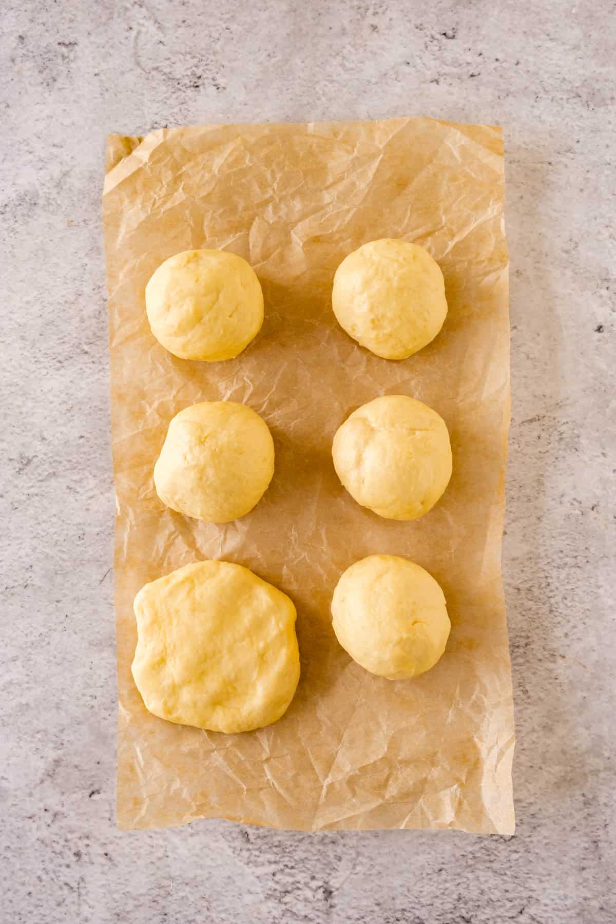 Brioche bread dough rolled into 6 balls on parchment paper. 