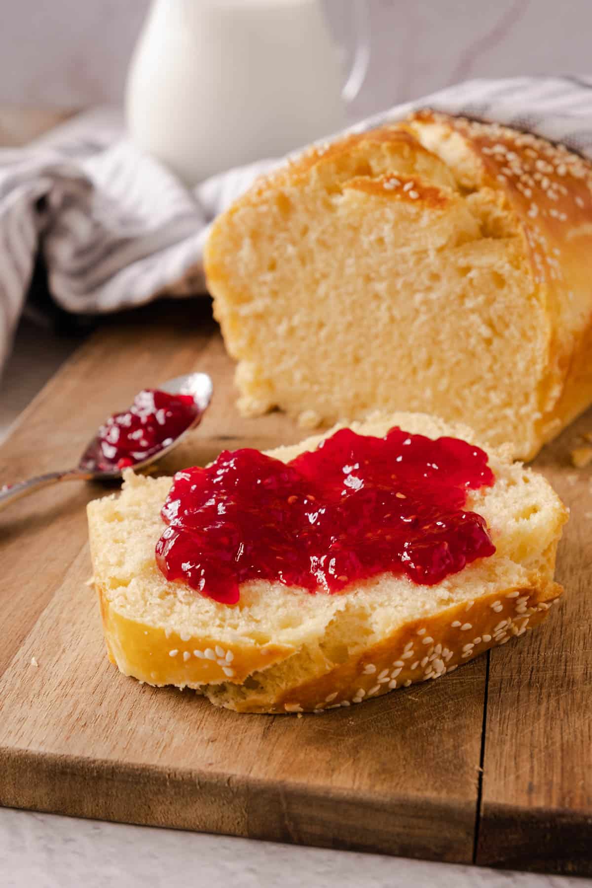 Jam spread over a slice of freshly baked brioche bread on a cutting board in front of the remaining loaf. 