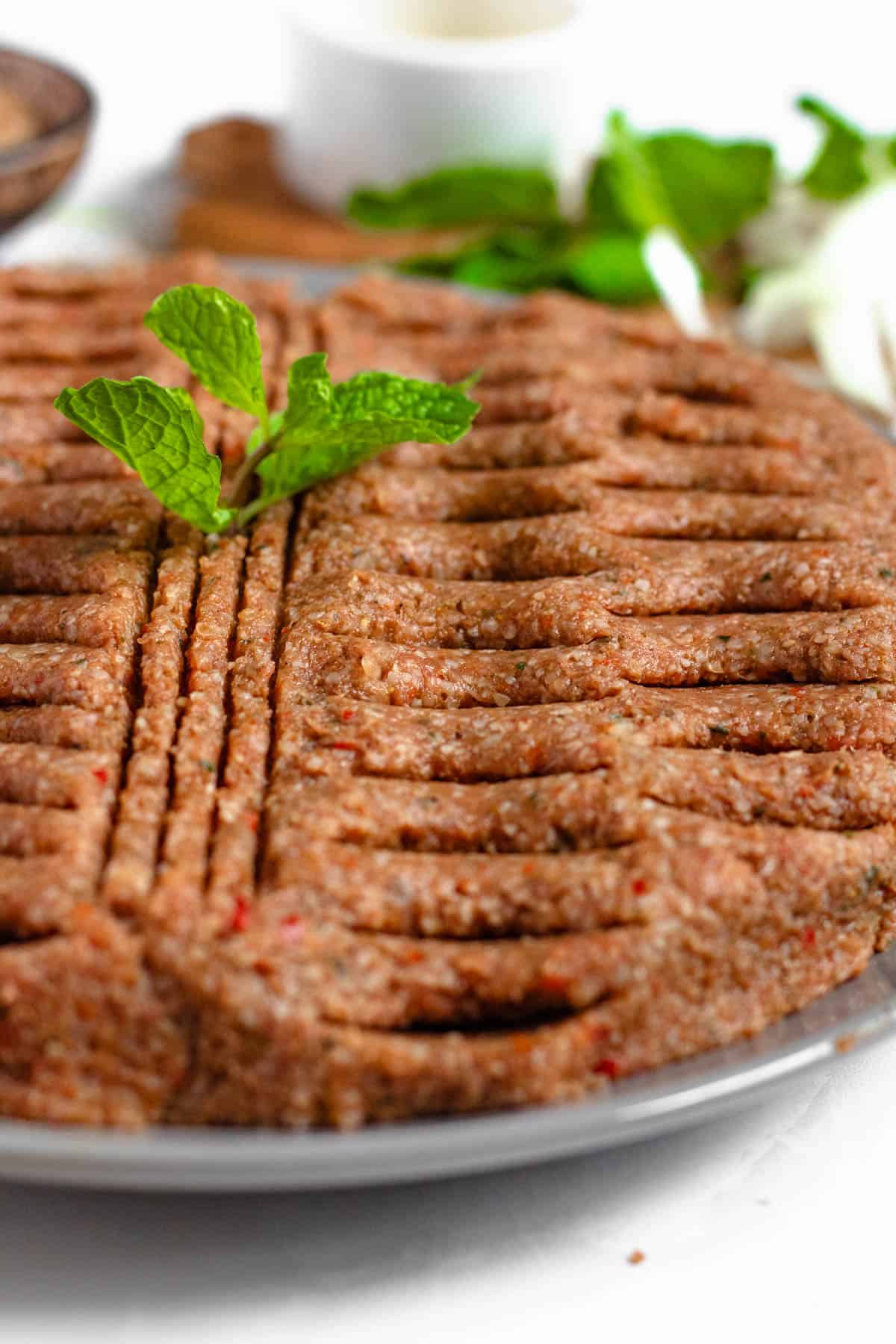 Kibbeh nayeh prepared on a serving dish, cut with slits for decoration with fresh mint garnished on the top. 