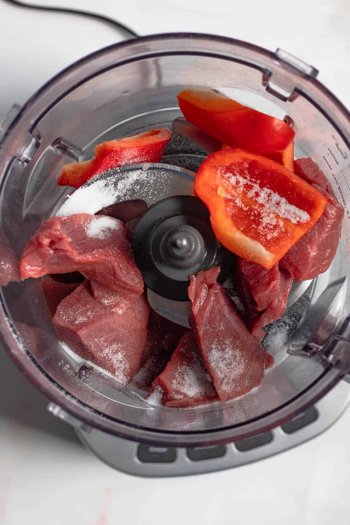 Beef and red bell peppers added to a food processor. 