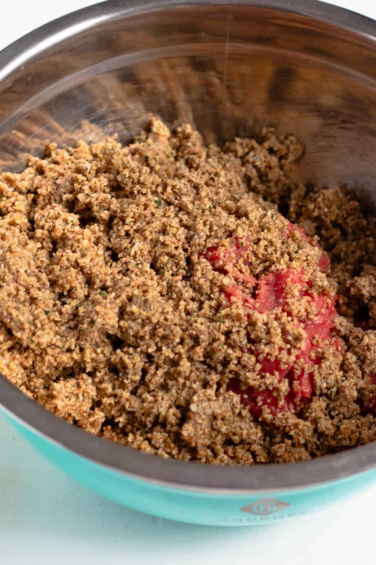 Meat mixture and soaked bulgur added to a mixing bowl. 
