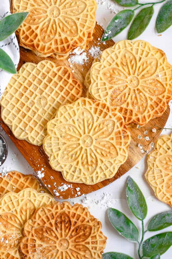 Freshly baked pizzelle are laying on a cutting board. 