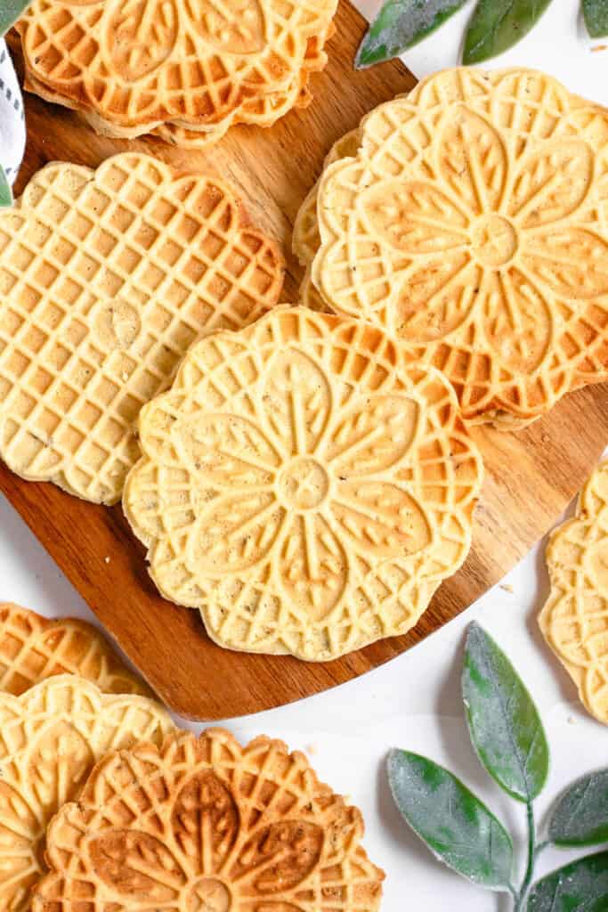 Freshly baked pizzelle are laying on a cutting board. 